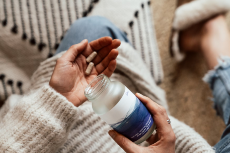 A woman pours supplements from a bottle into her hand.